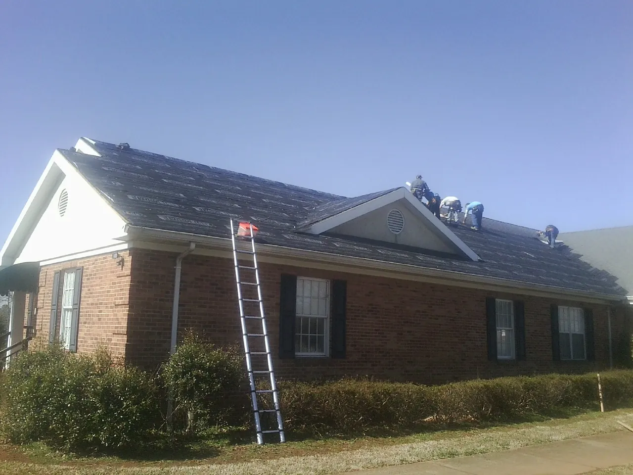 Crew tearing shingles off a brick ranch roof with a ladder set — Emergency Roof Repair work by our crew in Granite Falls