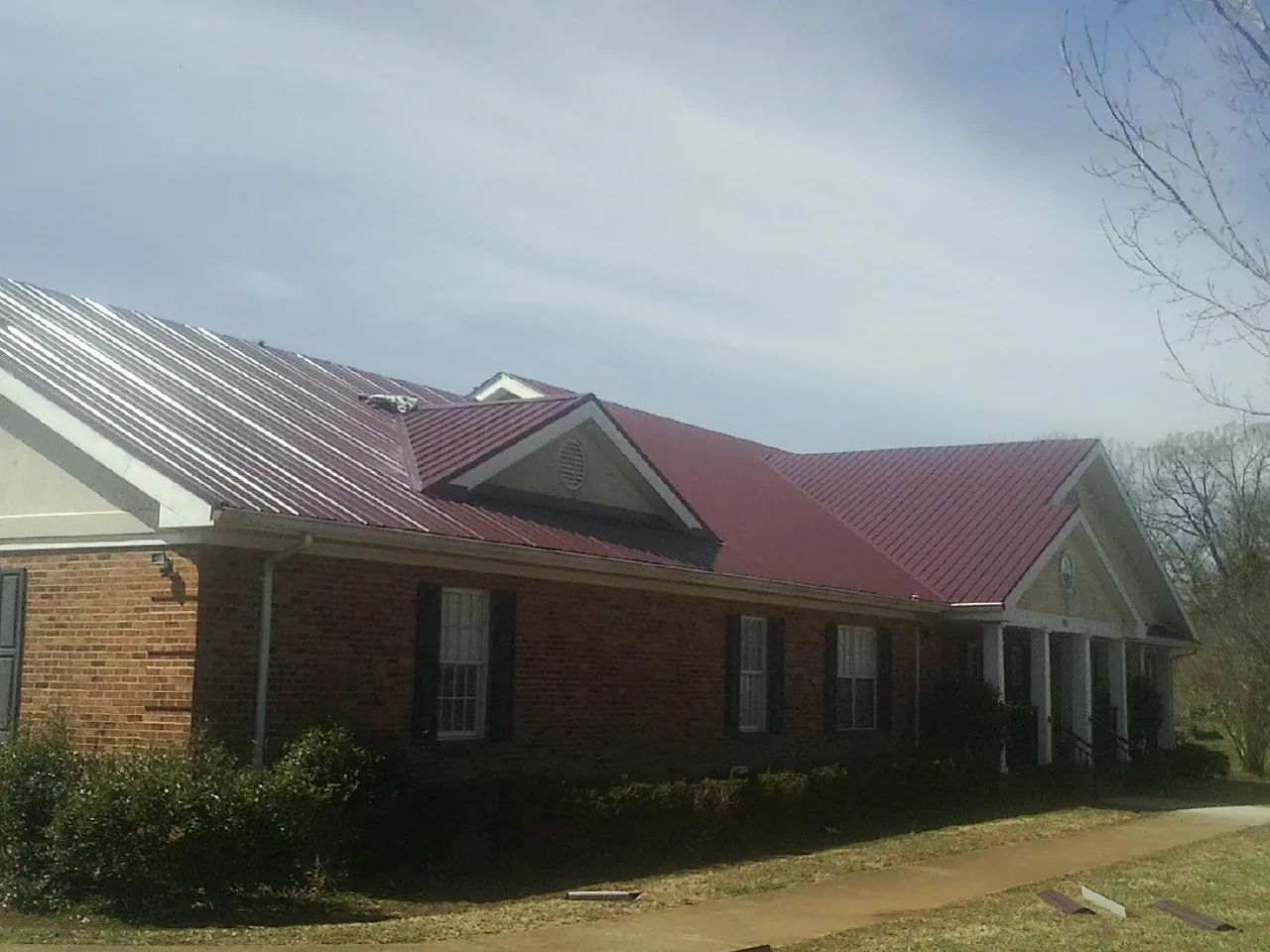 Red metal roof with gabled entries on a long brick building, from a Hail Damage Roof Repair job in Granite Falls