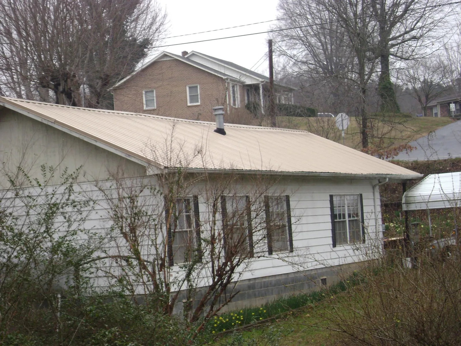 Tan metal roof on a white sided house set into a hillside — Commercial Roofing by Roofing Brothers in Granite Falls